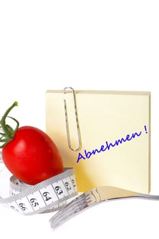 Sticky note with inscription: Slimming - Yellow notepad with the inscription: Slimming with paperclip behind a tomato with measuring tape and a fork against a white background