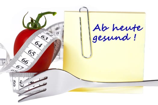 Sticky note with inscription: Healthy from today - Yellow notepad with the inscription: Healthy from today with paper clip behind a tomato with tape measure and a fork against a white background