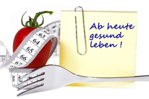 Sticky note with inscription: From today healthy living - Yellow notepad with the inscription: From today healthy living with paper clip behind a tomato with measuring tape and a fork against a white background