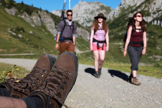 Three young people walking while hiking boots are visible at the edge