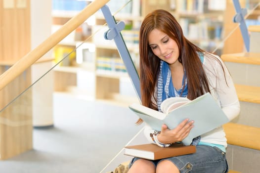 Teenage brunette student on high school library stairs reading book