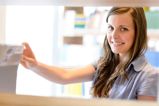 Young student woman choosing book among library shelves