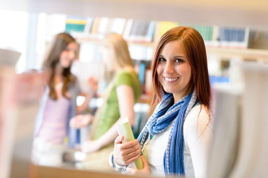 Young student woman choosing book among library shelves