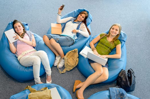 Young student girls resting on blue beanbags at library