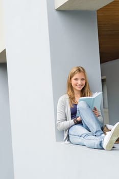 Happy young woman reading book outside of school smiling
