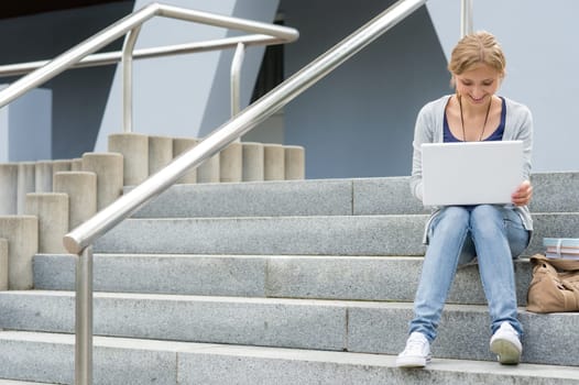Teenage girl working on laptop computer happy student on stairs