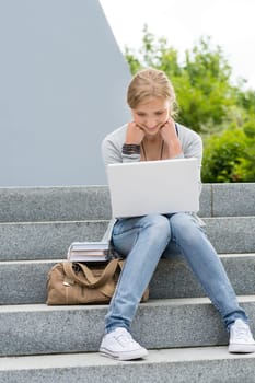 Young student woman outdoor with laptop sitting on stairs