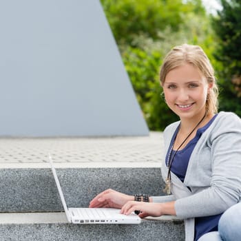 Teenage girl sitting on steps with laptop happy smiling student