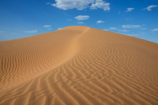 Sahara desert sand dune with cloudy blue sky at Erg Lihoudi, M&#039 hamid, Morocco