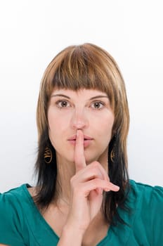 Head and shoulders shot of a young woman holding her finger in front of her mouth (gesture: Psst!) Looking at the camera