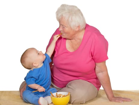 A tender moment as an adorable small baby reaches up with a biscuit to place it in the grandmothers mouth as the two sit on a carpet on the floor