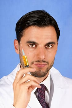 Handsome doctor holding a syringe with yellow liquid. Over a light blue background.