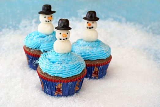 Chocolate cupcakes with vanilla frosting decorated with snowmen made of fondant and rolled in sugar.
