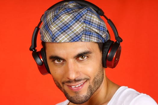 Smiling 30 years old man with beret and earphones over an orange background