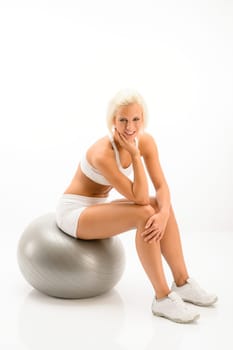 Smily blonde sitting on silver pilates ball on white background