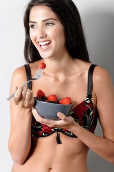 Beautiful young woman in underwear leaning against a wall enjoying a fruit salad