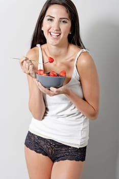 Beautiful young woman in underwear leaning against a wall enjoying a fruit salad
