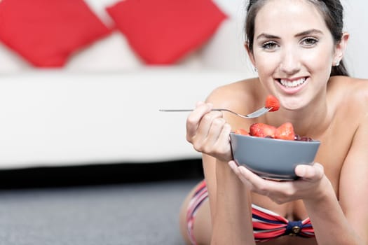 Beautiful young woman enjoying fresh fruit for breakfast in a red bikini