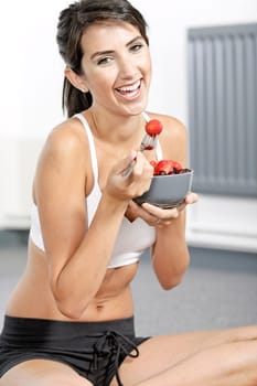 beautiful young woman in fitness clothes eating fresh fruit from a bowl at home