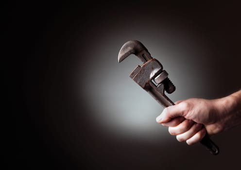 A man&#039 s hand holding a pipe wrench highlighted against a black background