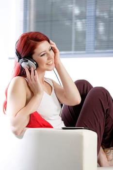 Happy smiling young woman listening to music at home on headphones