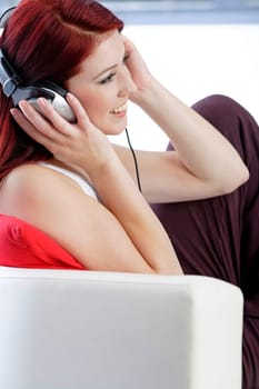 Happy smiling young woman listening to music at home on headphones