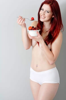 Happy young woman eating a bowl of fresh fruit in her underwear at home