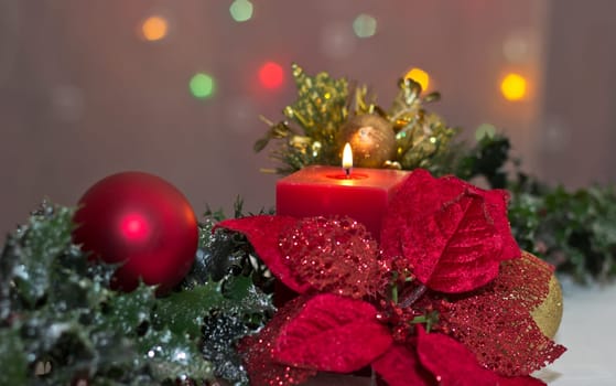A bright red poinsetta with a christmas candle and holly