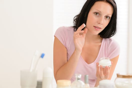 Beauty woman putting facial cream in front of bathroom mirror