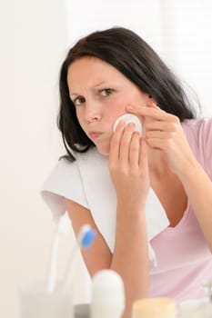 Young brunette woman in bathroom squeezing pimple cleaning acne skin