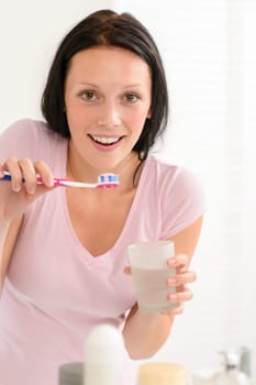 Young brunette woman brushing teeth with toothpaste holding glass water