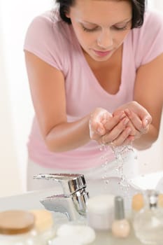 Woman washing face with water above bathroom sink