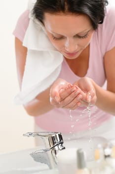 Woman washing face with water above bathroom sink