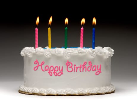 White birthday cake profile on graident background with five colorful lit candles and "Happy Birthday"" written on the side with frosting"