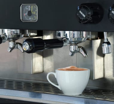 Coffee cup filled with cappuccino coffee, sitting on the tray of a commercial espresso machine