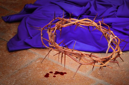 Crown of thorns as worn by Christ during the crucifixion against a purple robe and pavement tiles