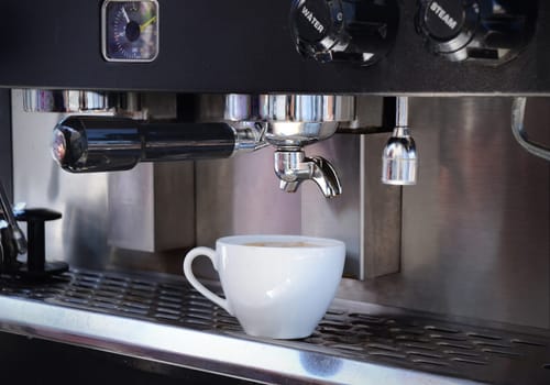 Coffee cup filled with cappuccino coffee, sitting on the tray of a commercial espresso machine
