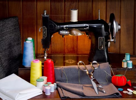 Retro sewing machine with sewing paraphernalia including thread, fabric, sewing needles, pin cushion, buttons scissors and thimble