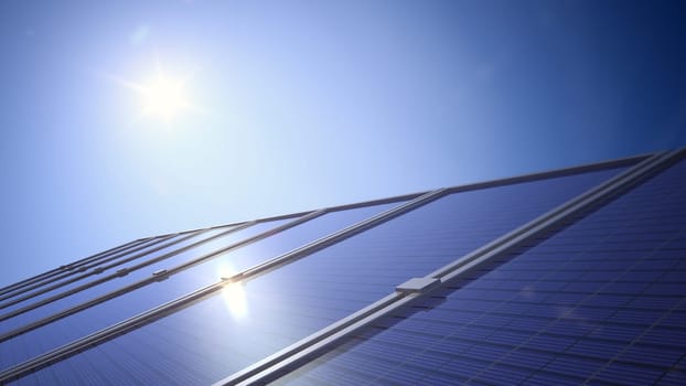 Close-up of a solar panel showing the sun in a clear deep blue sky with reflection off the panel.