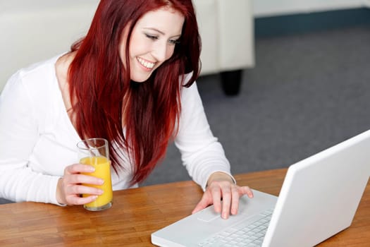 Beautiful young woman using a laptop at home with a fresh glass of Orange juice.