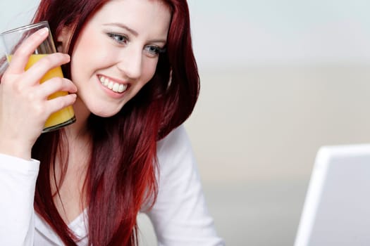Beautiful young woman using a laptop at home with a fresh glass of Orange juice.