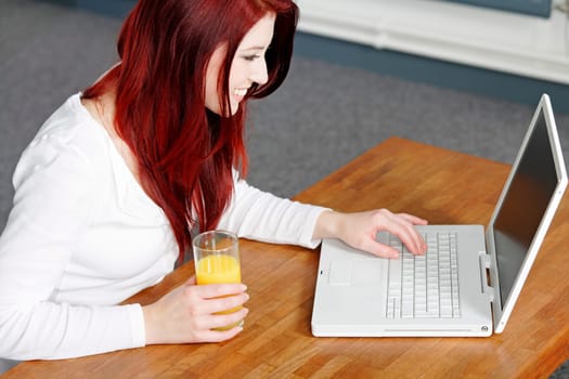 Beautiful young woman using a laptop at home with a fresh glass of Orange juice.