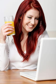 Beautiful young woman using a laptop at home with a fresh glass of Orange juice.