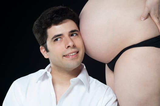 Portrait of young father listening to baby belly and smiling.