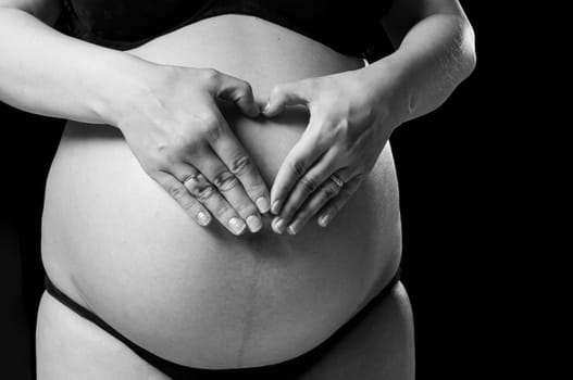 Cropped shot of woman making shape of heart on baby belly.
