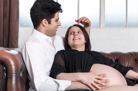 Young couple sitting on sofa in home setting, enjoying pregnancy.