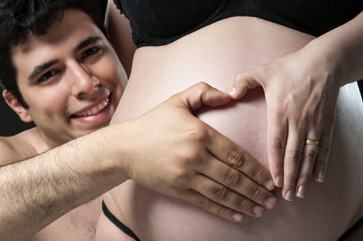 Portrait of young father making the shape of a heart on woman&#039 s baby belly and smiling.
