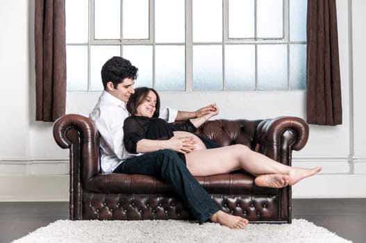 Young couple sitting on sofa in home setting, enjoying pregnancy.