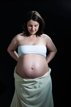 Portrait of happy young pregnant woman looking at her baby belly.