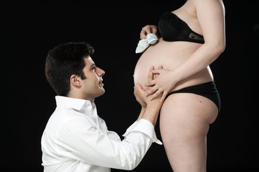 Portrait of young father looking at baby shoes on wife&#039 s baby belly.